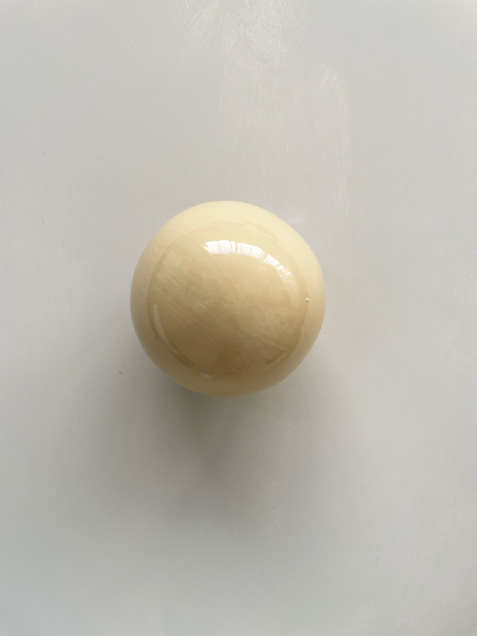 Handcrafted ceramic ball wall sculpture in butter color reflecting light.