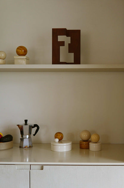 Medium ceramic box 'BOULE' in vanilla and cognac on a shelf in a stylish home setting.