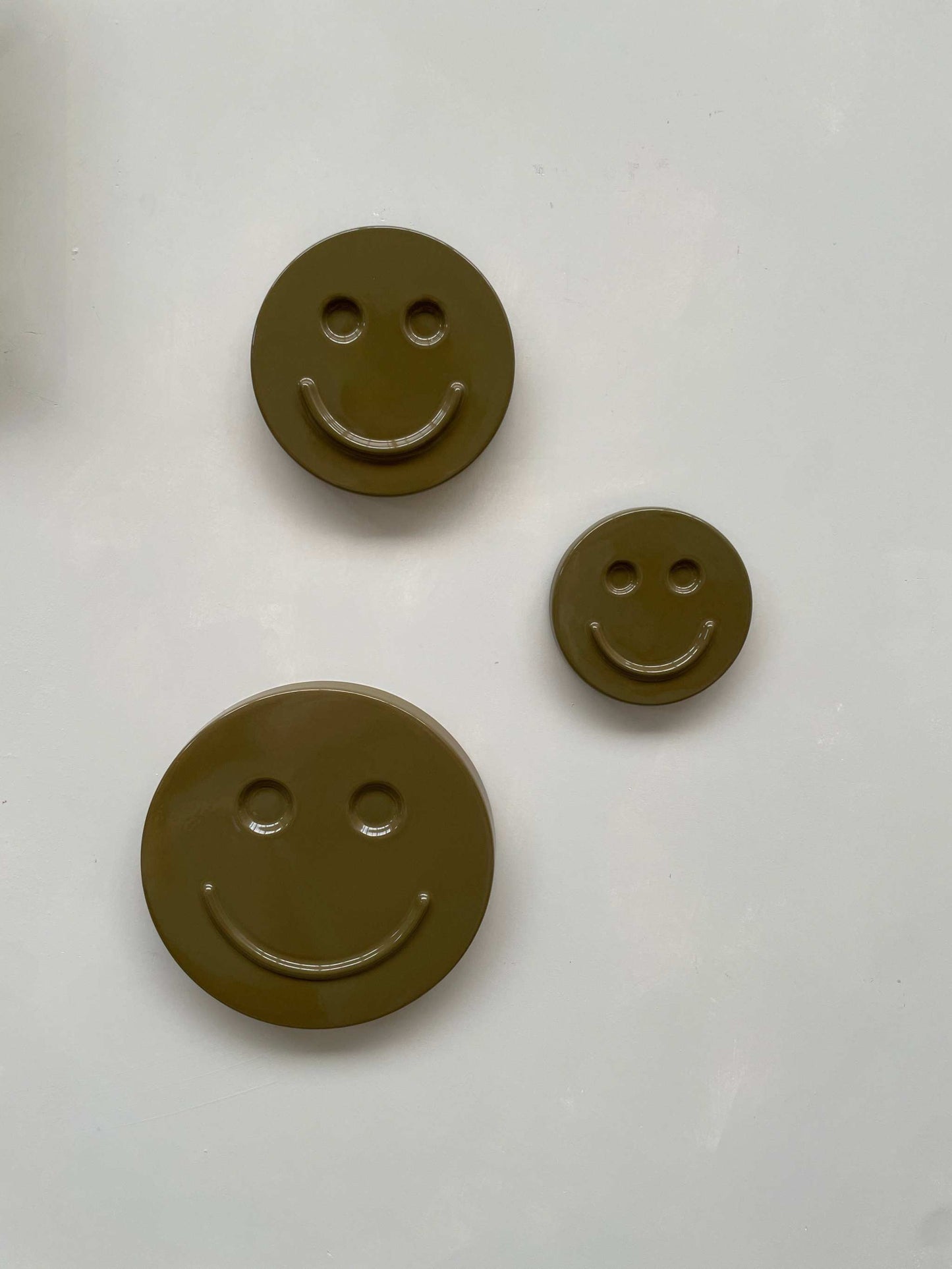 Olive 'HAPPY' ceramic artwork with three smiley face designs in different sizes.