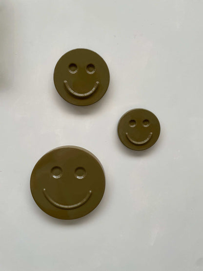 Olive 'HAPPY' ceramic artwork with three smiley face designs in different sizes.