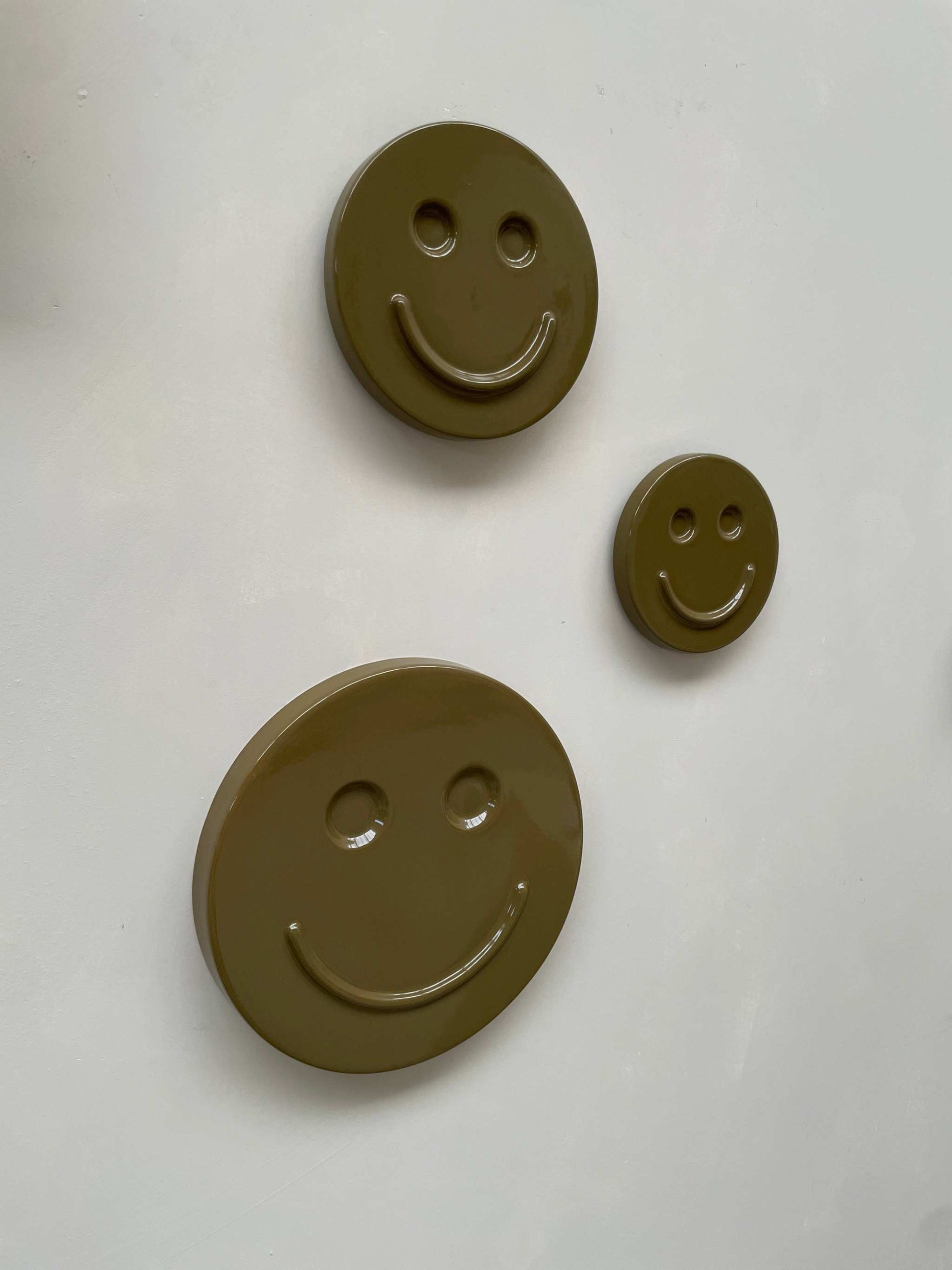 Olive 'HAPPY' ceramic artwork with smiling face design in three sizes.