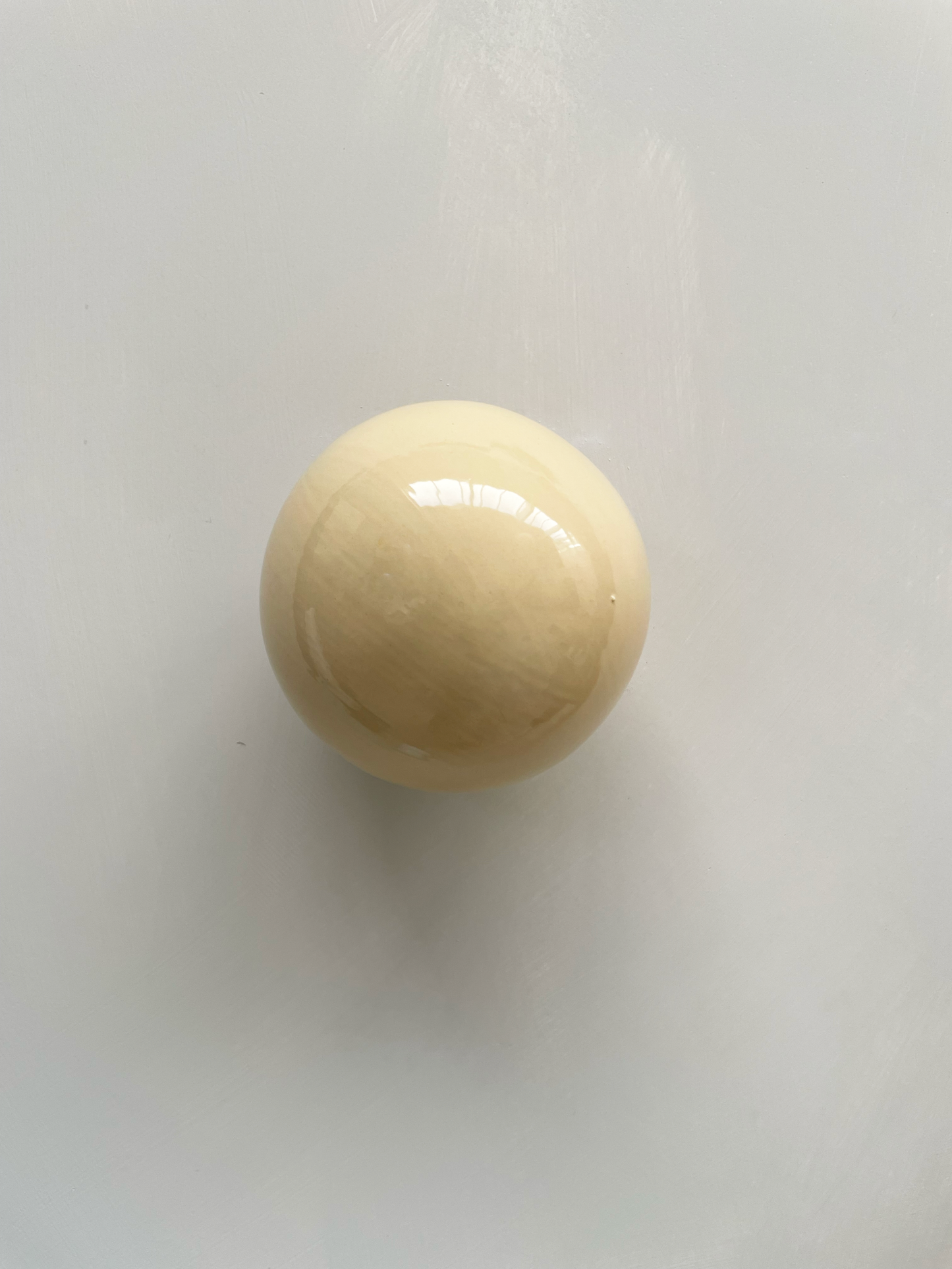 Handcrafted ceramic ball wall sculpture in butter color reflecting light.