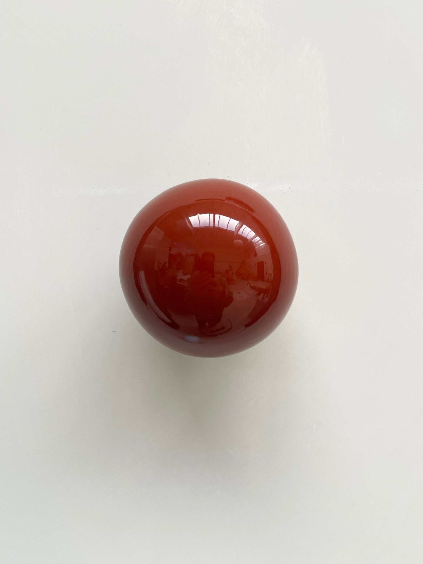 Ceramic ball in rust burgundy color, handcrafted wall sculpture reflecting light and shadows.