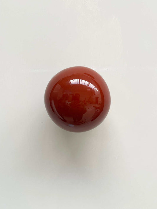 Ceramic ball in rust burgundy color, handcrafted wall sculpture reflecting light and shadows.