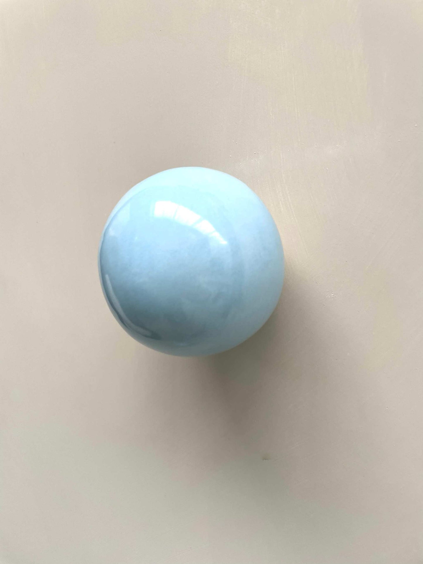 Handcrafted ice blue ceramic ball wall sculpture reflecting light.