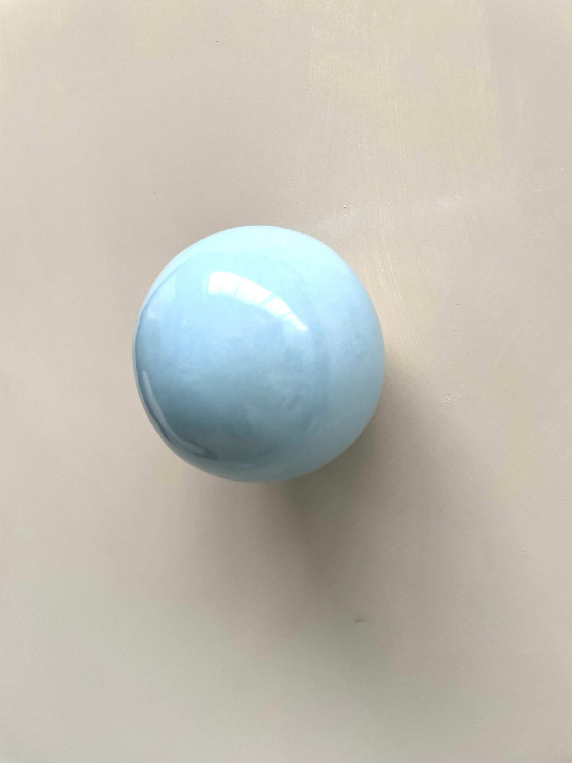 Handcrafted ice blue ceramic ball wall sculpture reflecting light.