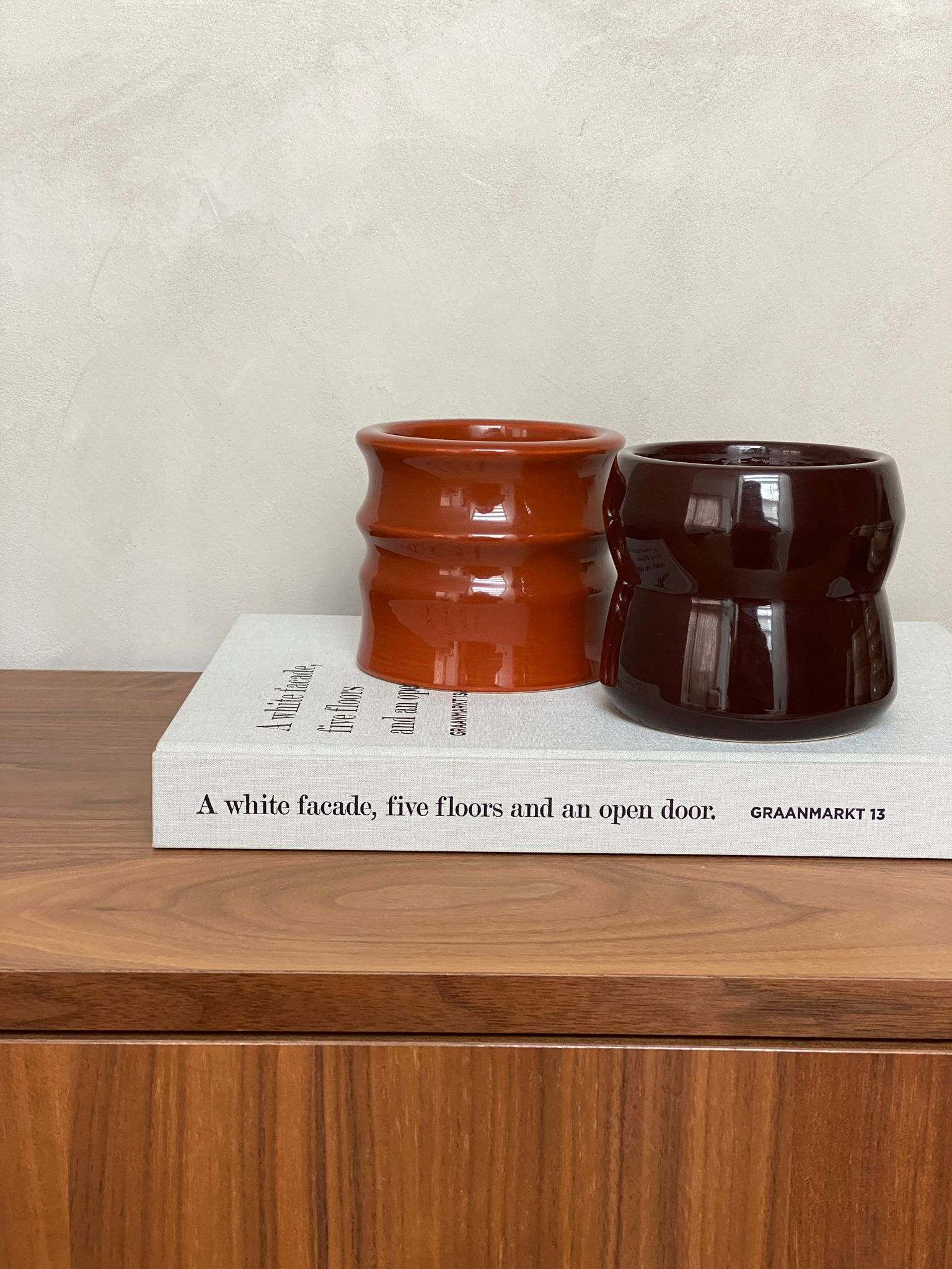 Scented candles in aubergine ceramic holders, featuring Shape 02 design, displayed on a wooden surface with a book.