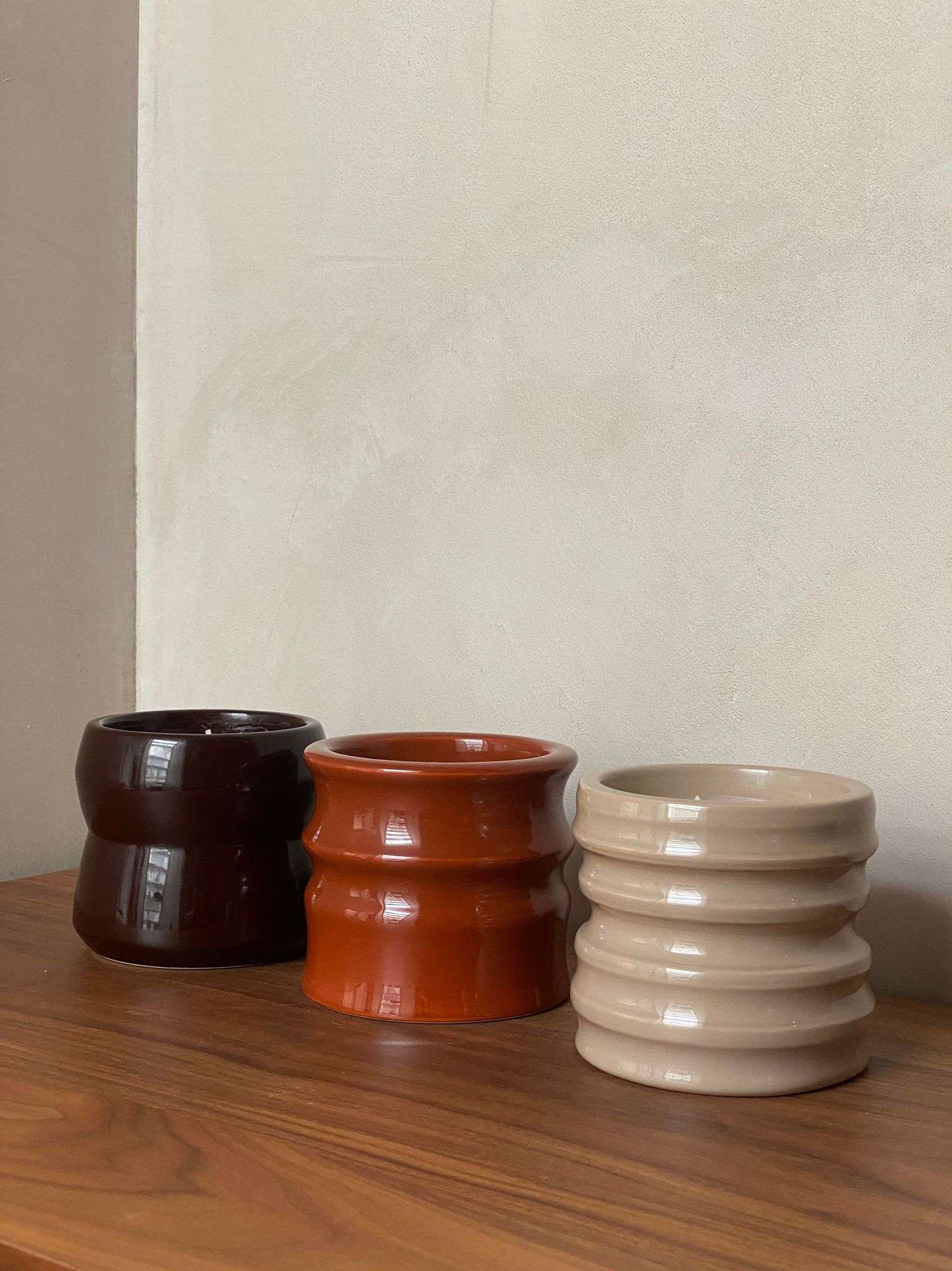 Shape 01.02 Terra scented candle holders in shades of brown, terracotta, and beige on a wooden surface.