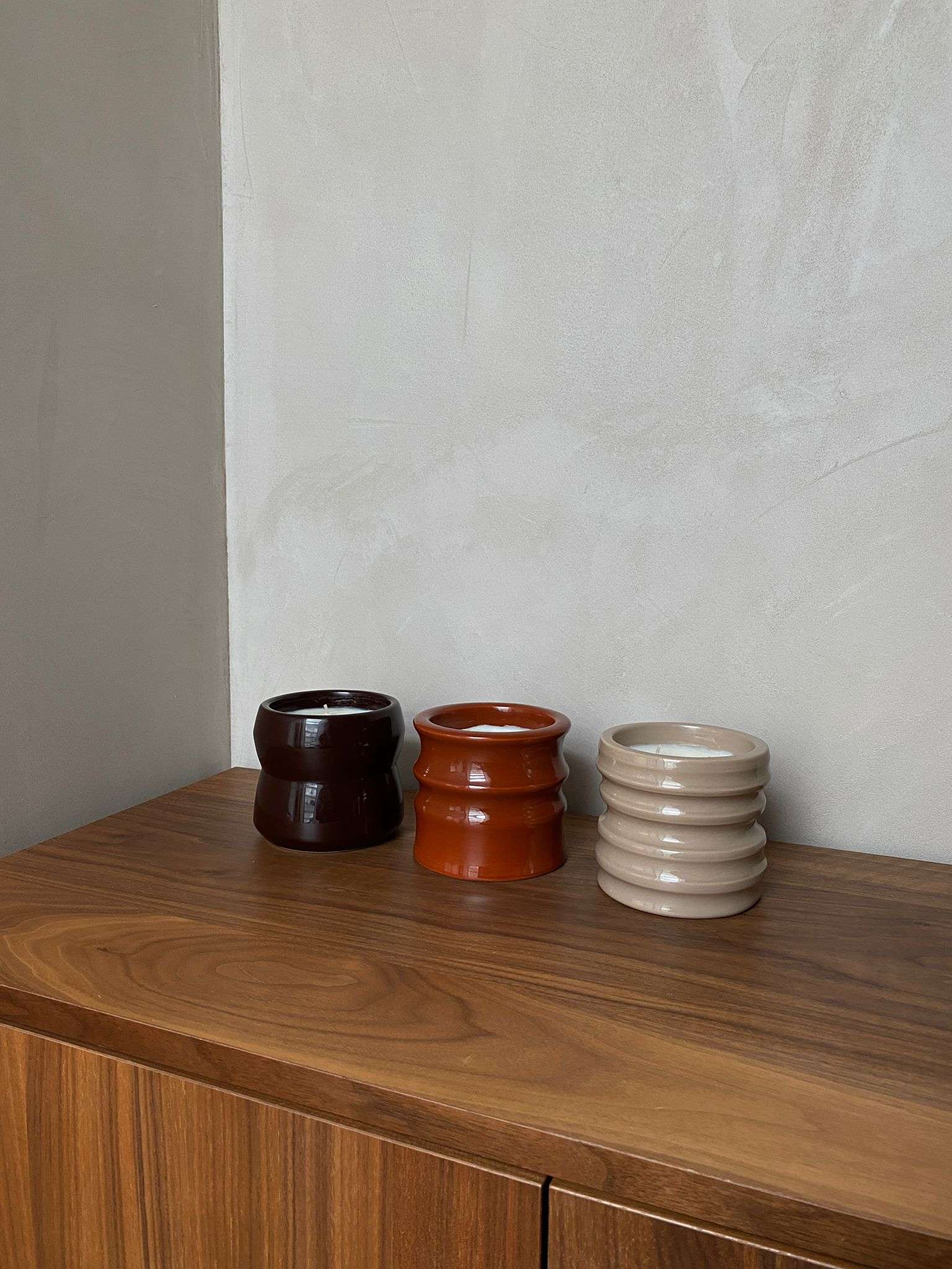 Scented candles in unique handcrafted ceramic holders on a wooden surface, part of the Shape 01.02 Terra collection.