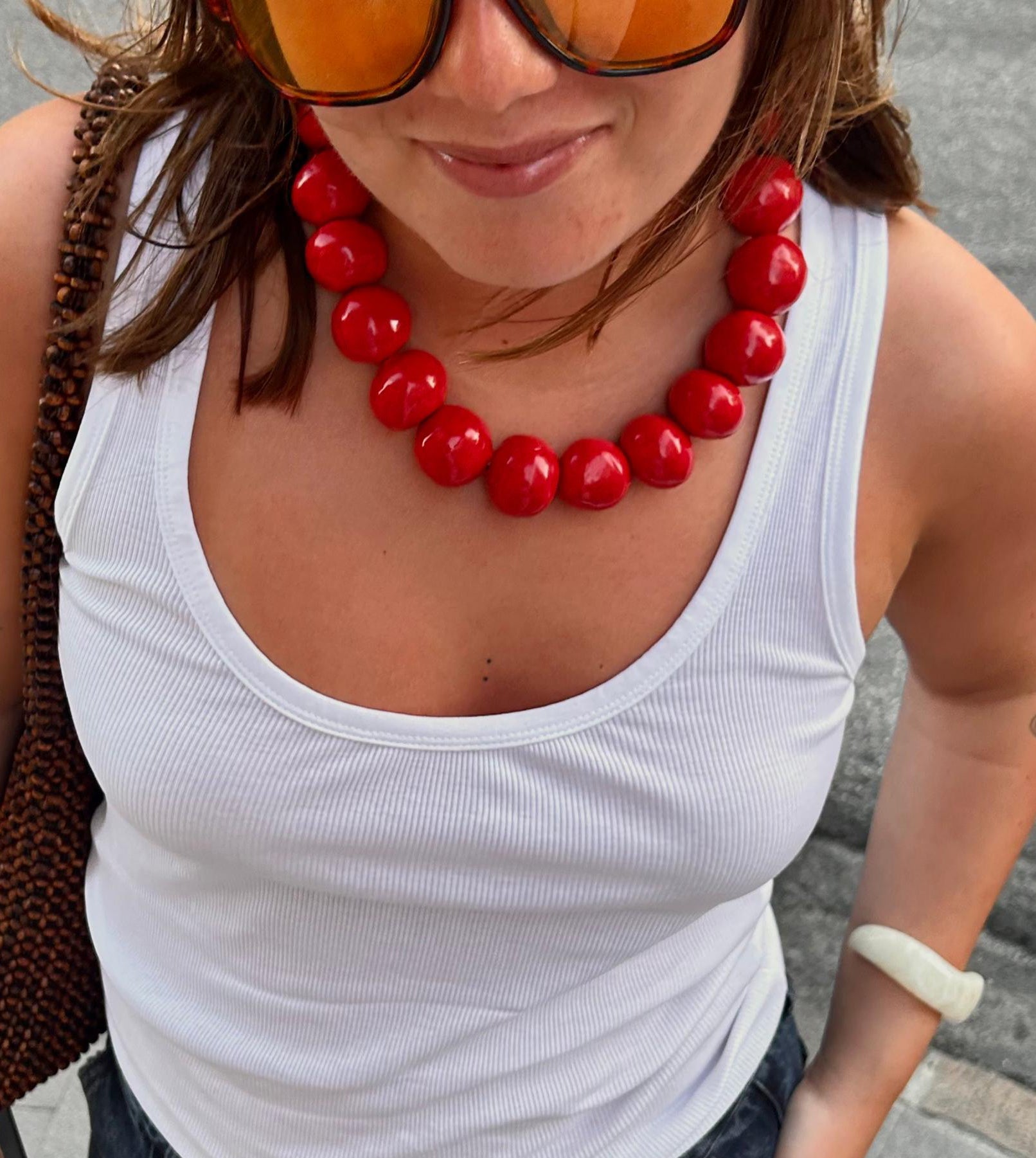 Woman wearing handmade ceramic bead necklace with large glossy red beads and white tank top