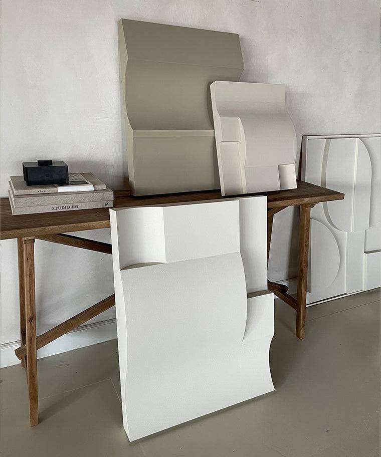 Modern art sculptures in neutral tones on a wooden table, featuring hand-made designs with a smooth sand-textured surface.