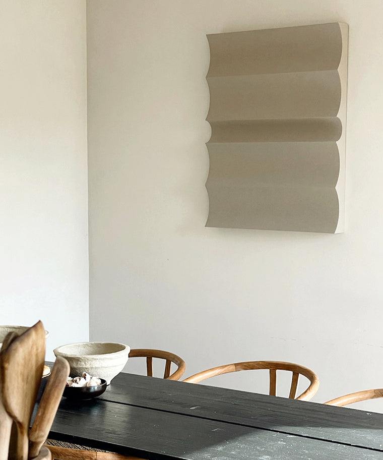 3D art piece '#22.04 Dunes' with sand texture, made from plant-based PLA, displayed on a wall above a wooden dining table.
