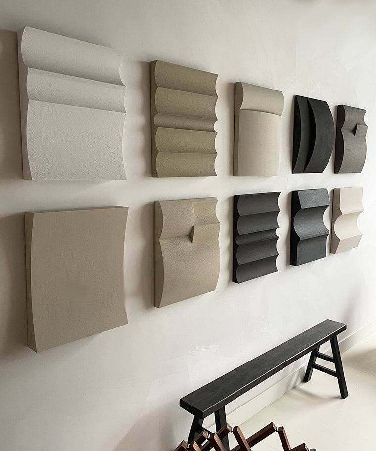 Hand-made art pieces on wall display, featuring various textured designs made from biodegradable PLA with sand texture and eco-paint, in neutral tones.