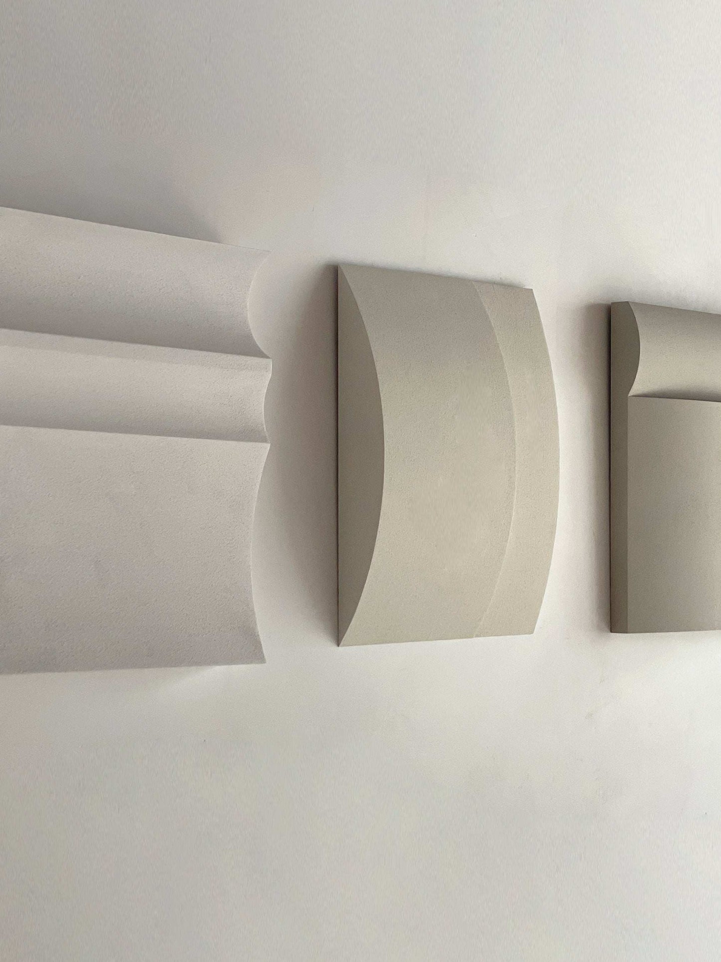 Contemporary wall art in white, shadow white, dark lime, brown wood, and mud grey tones displayed on a wall.